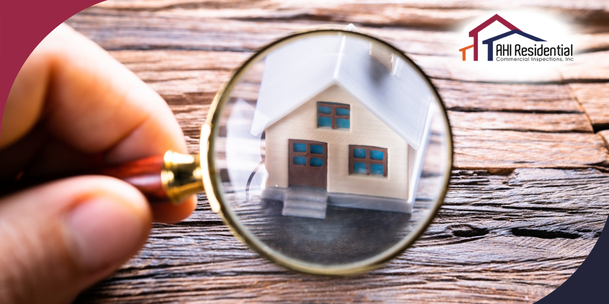 AHI Residential & Commercial Inspections A close-up image of a hand holding a magnifying glass over a small house model