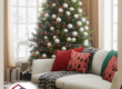 A warmly decorated living room featuring a Christmas tree adorned with ornaments, festive pillows on a cozy sofa, and wrapped presents near a window.