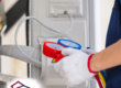A home inspector in a plaid shirt and overalls performs an HVAC inspection using colorful pressure gauges.
