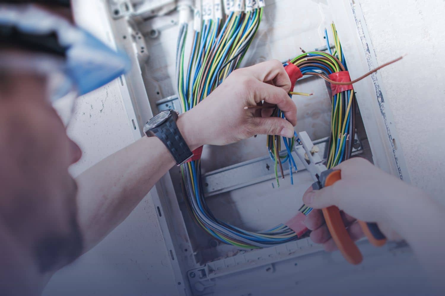Home 35 Close-up of an electrician using pliers to strip and organize colorful electrical wires inside an open circuit breaker panel.
