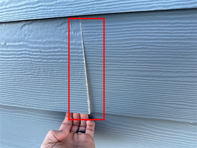 Inspector's hand showing a gap and buckle at a fiber cement siding joint on Home C