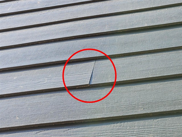 Damaged and misaligned fiber cement siding board on Home D
