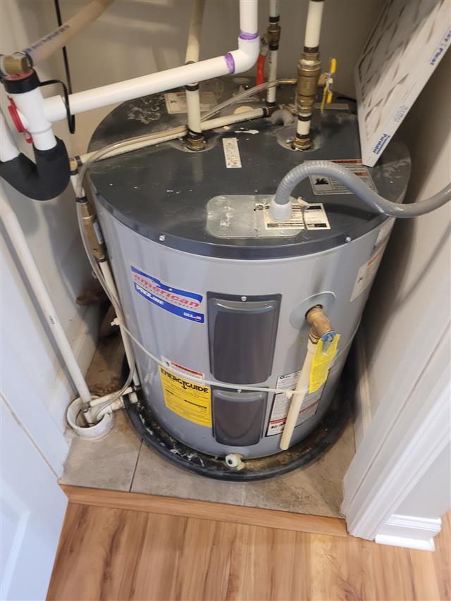 Electric water heater in a condo closet with rust staining and debris in the drain pan