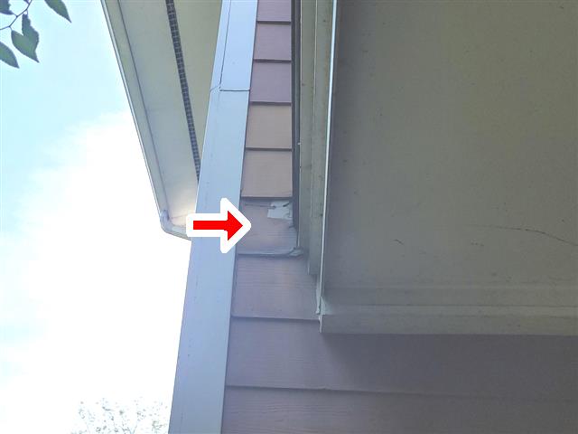 Damaged siding at a roof-to-wall junction near a gutter on a condo building